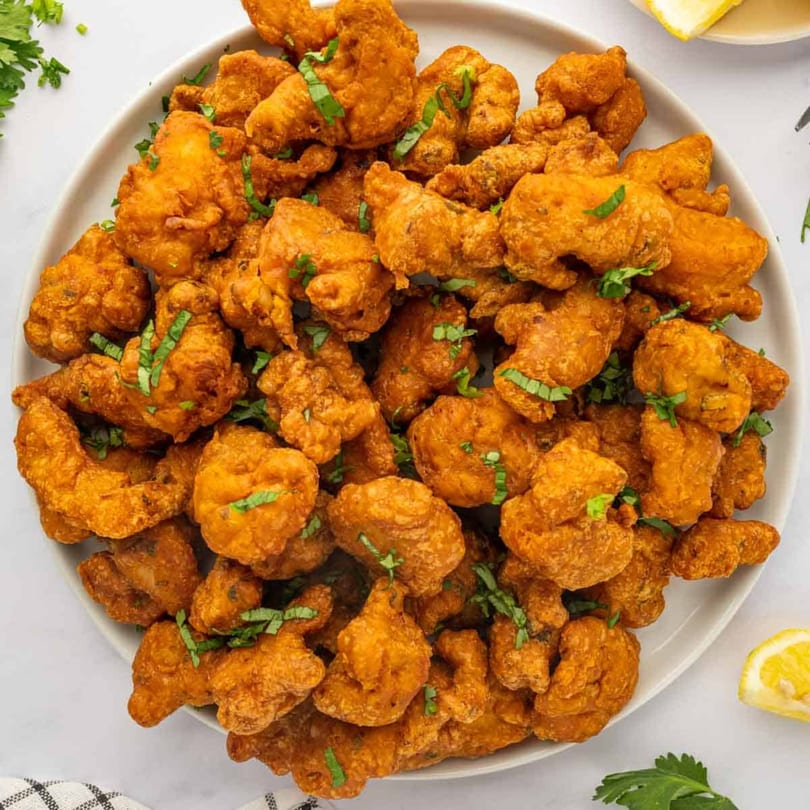 A large platter of golden-brown Indian pakora, garnished with fresh green herbs and lemon wedges.
